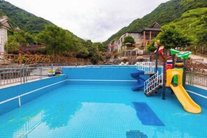 Una piscina con tobogán y zona vallada, rodeada de vegetación y edificios.
