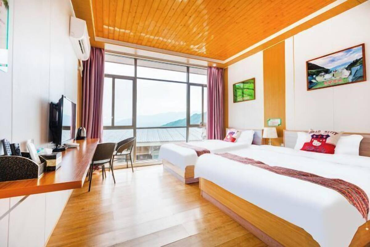 A hotel room with a wooden ceiling, large windows, a desk, two beds, and artwork on the walls.