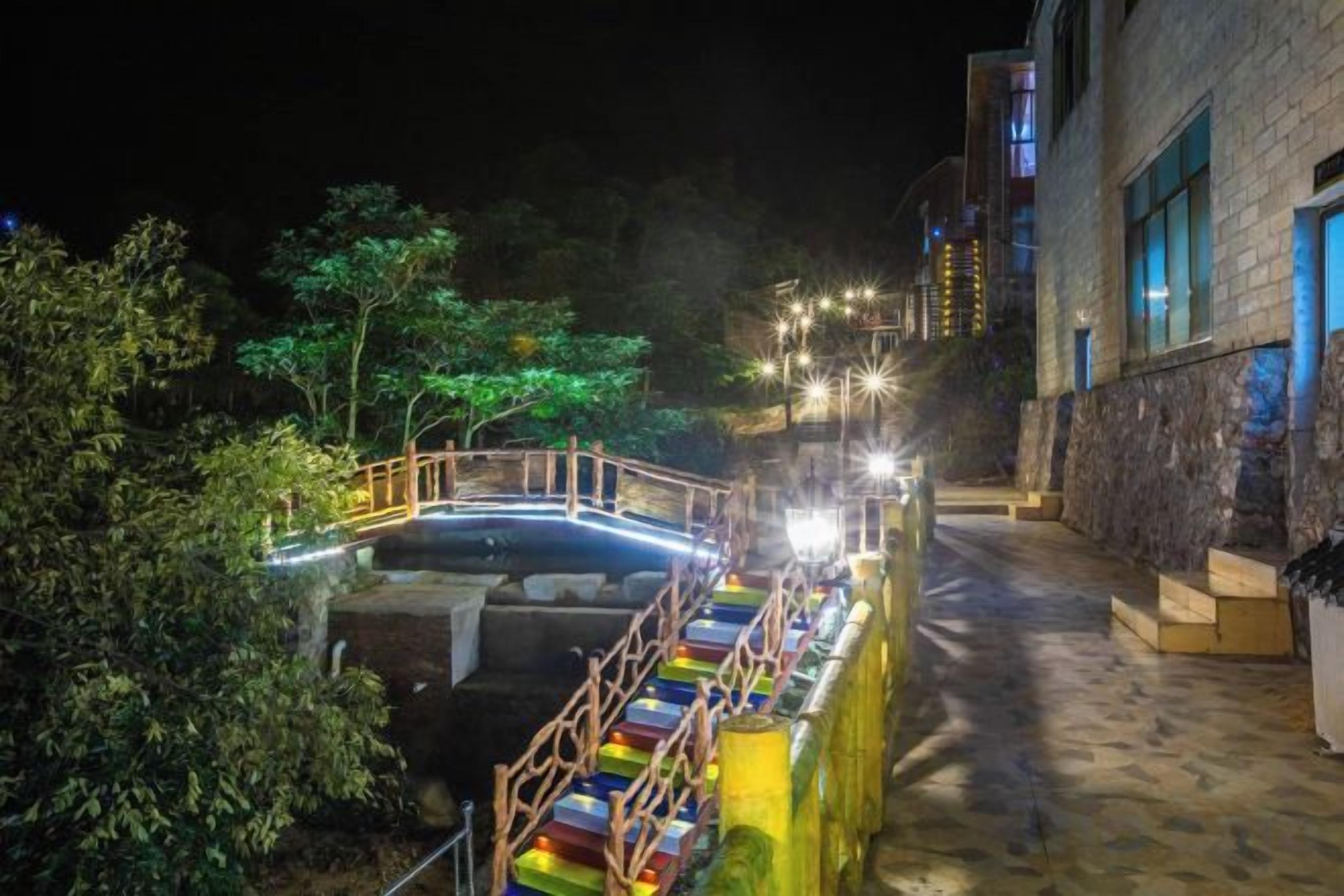 Vista nocturna de un edificio con fachada de piedra, un puente de madera y un camino pavimentado.