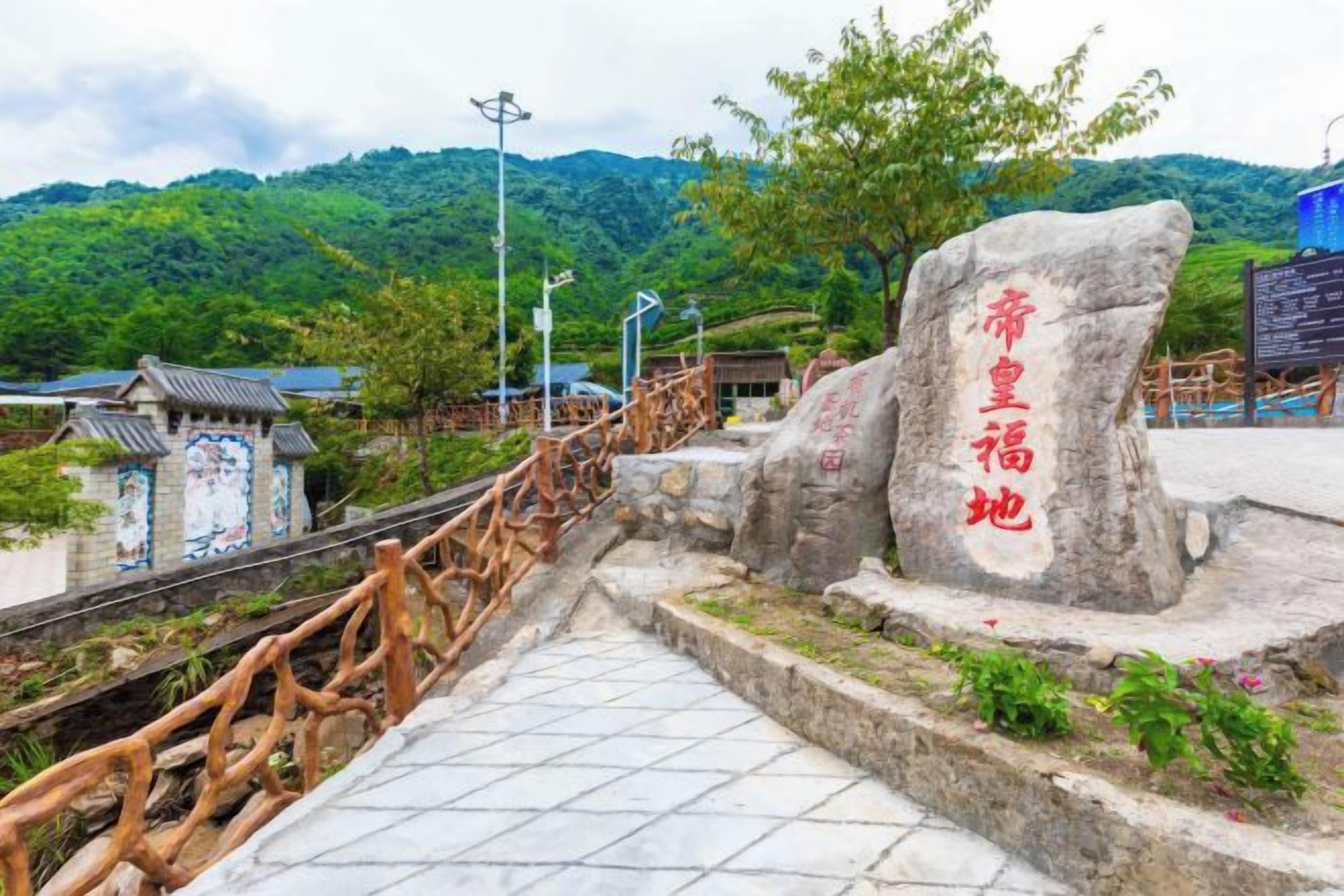 A stone monument with inscriptions, a wooden fence, and a tiled pathway leading to a traditional building.