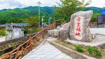 A stone monument with inscriptions, a wooden fence, and a tiled pathway leading to a traditional building.