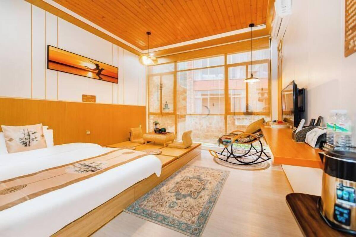 A hotel room with a bed, a rocking chair, a TV, and a kitchen area.
