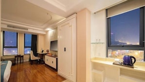 A hotel room with a wooden floor, a desk, a chair, a bed, a wardrobe, a window with a city view, and a shelf with a kettle. - nanyuan e home hotel (liu an Railway Station Hotel ) ) (Lu'an)