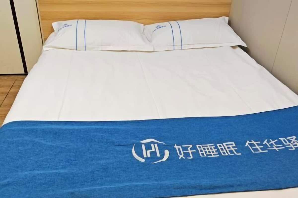 A neatly made bed with white linens and a blue blanket featuring a logo.