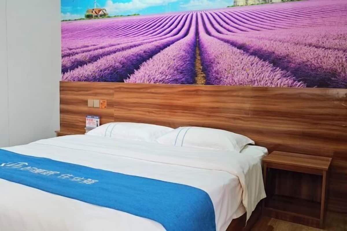 A hotel room with a bed, a wooden headboard, and a wall mural of lavender fields.