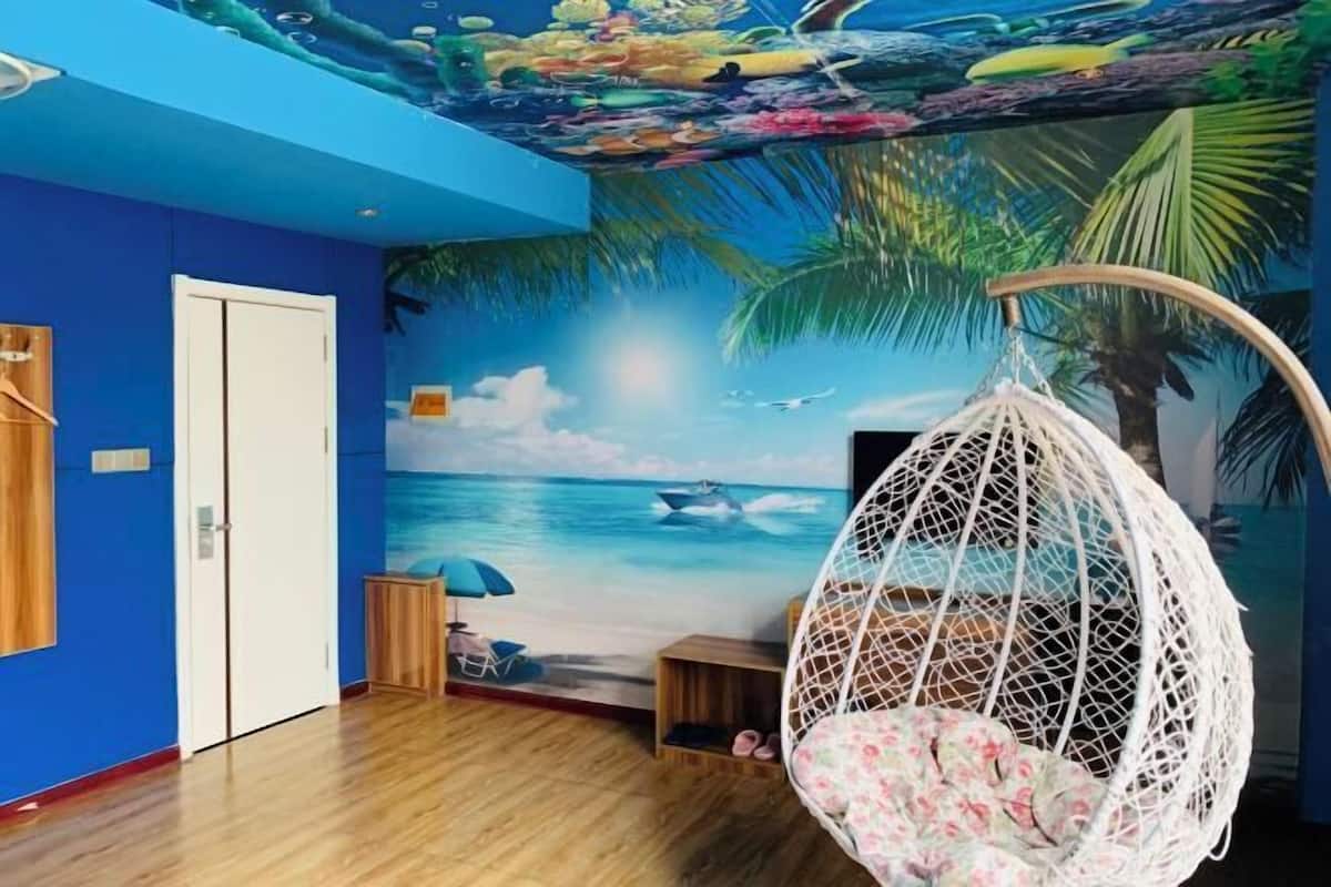 A room with a blue wall, a mural of a beach scene, a white hanging chair, and a wooden door.