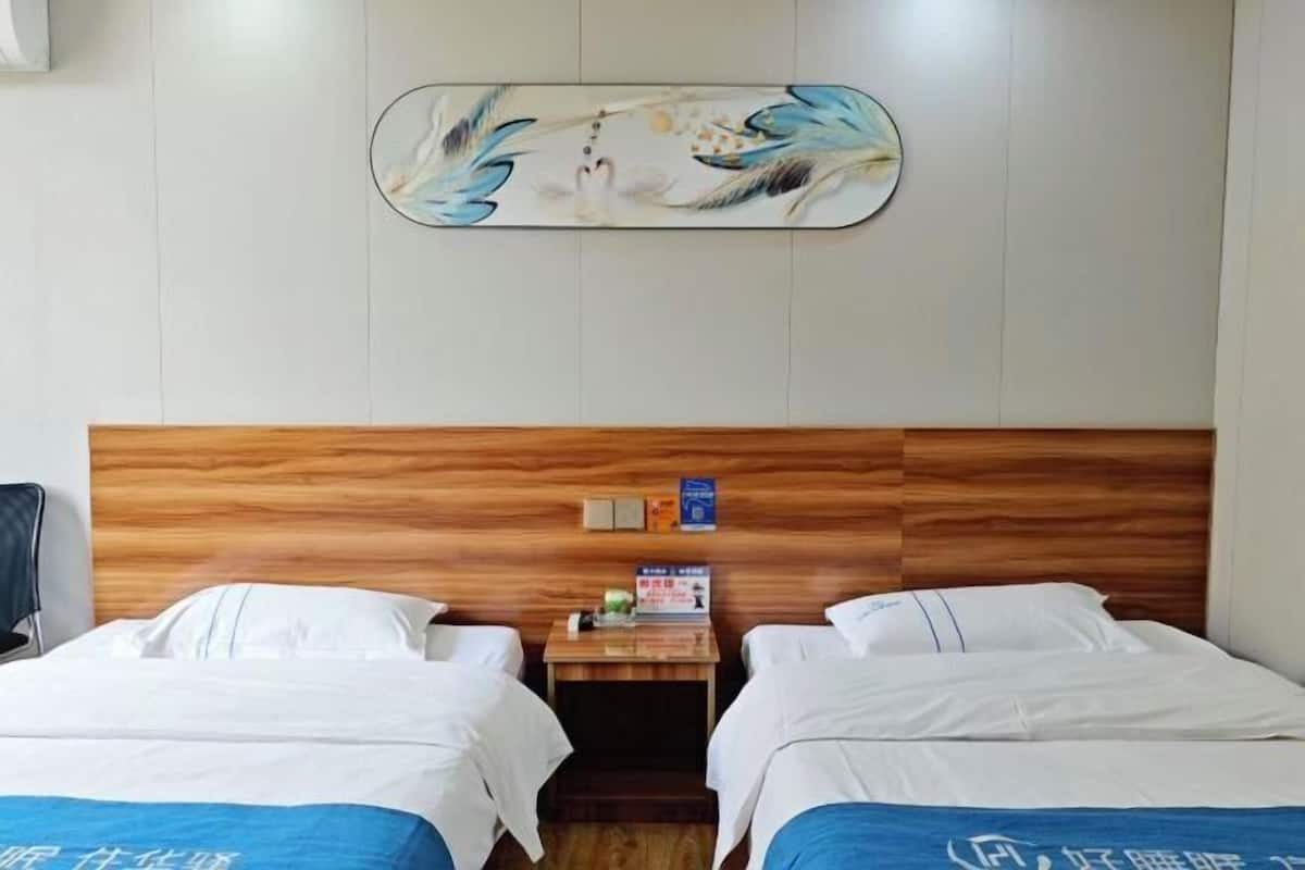A hotel room with two beds, a wooden headboard, a small table with a sign, and a wall-mounted artwork.