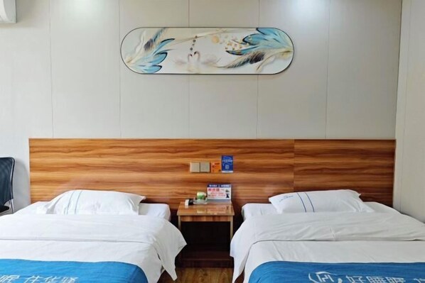 A hotel room with two beds, a wooden headboard, a small table with a sign, and a wall-mounted artwork.