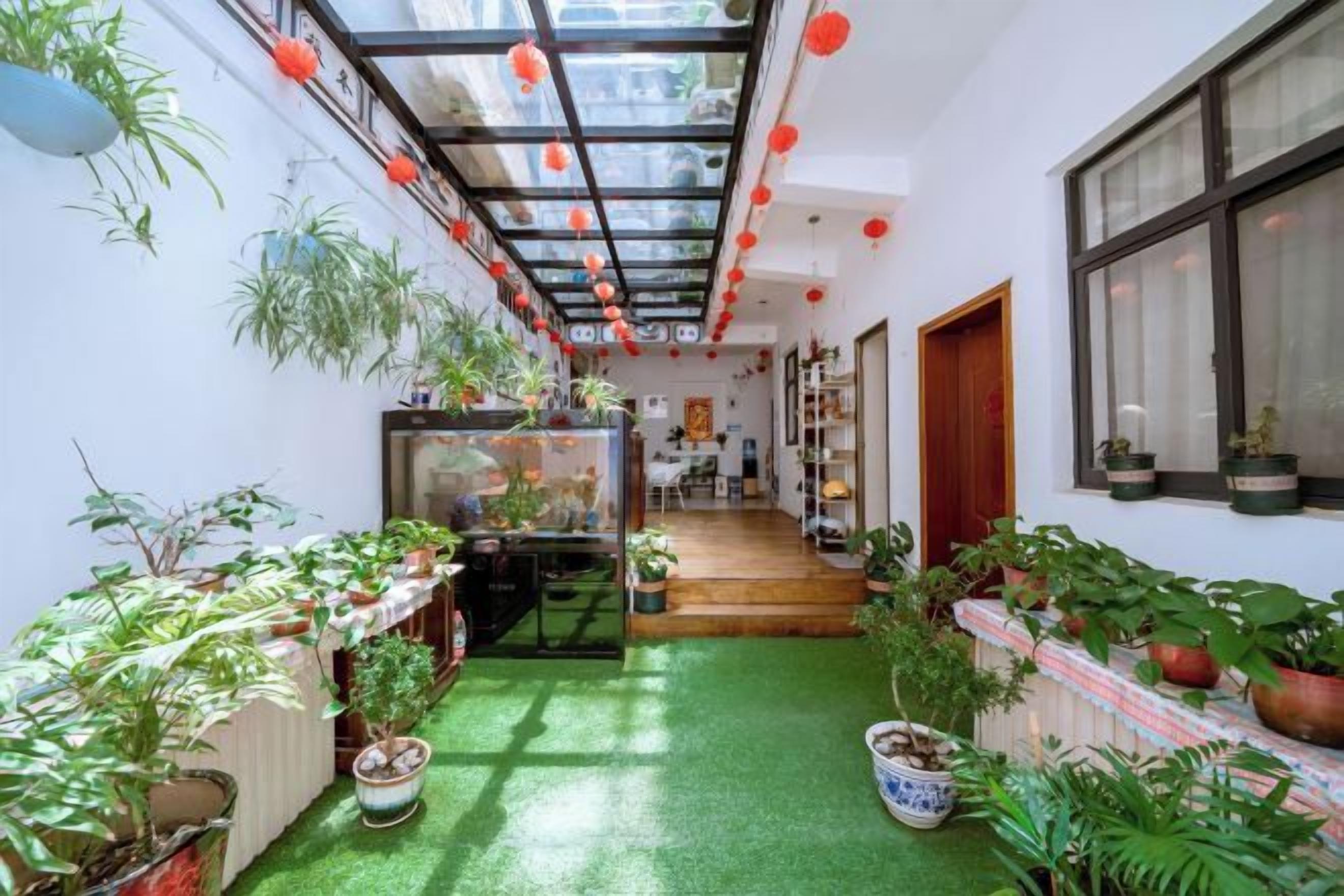 A narrow indoor space with a green artificial turf floor, potted plants, and a glass ceiling.
