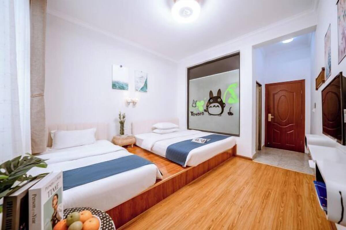A hotel room with two beds, a wooden floor, a large mirror with a cartoon character, and a door.
