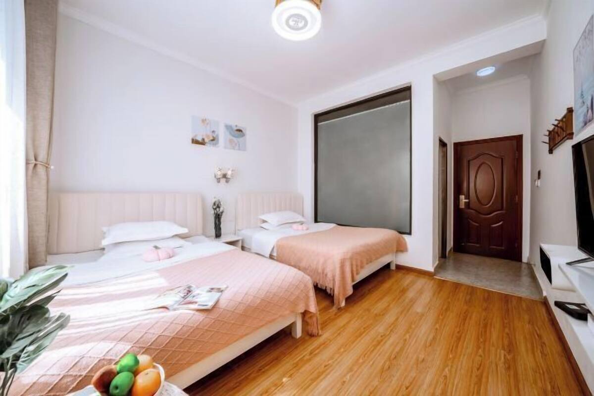 A bedroom with two beds, a large mirror, a TV, and a wooden floor.