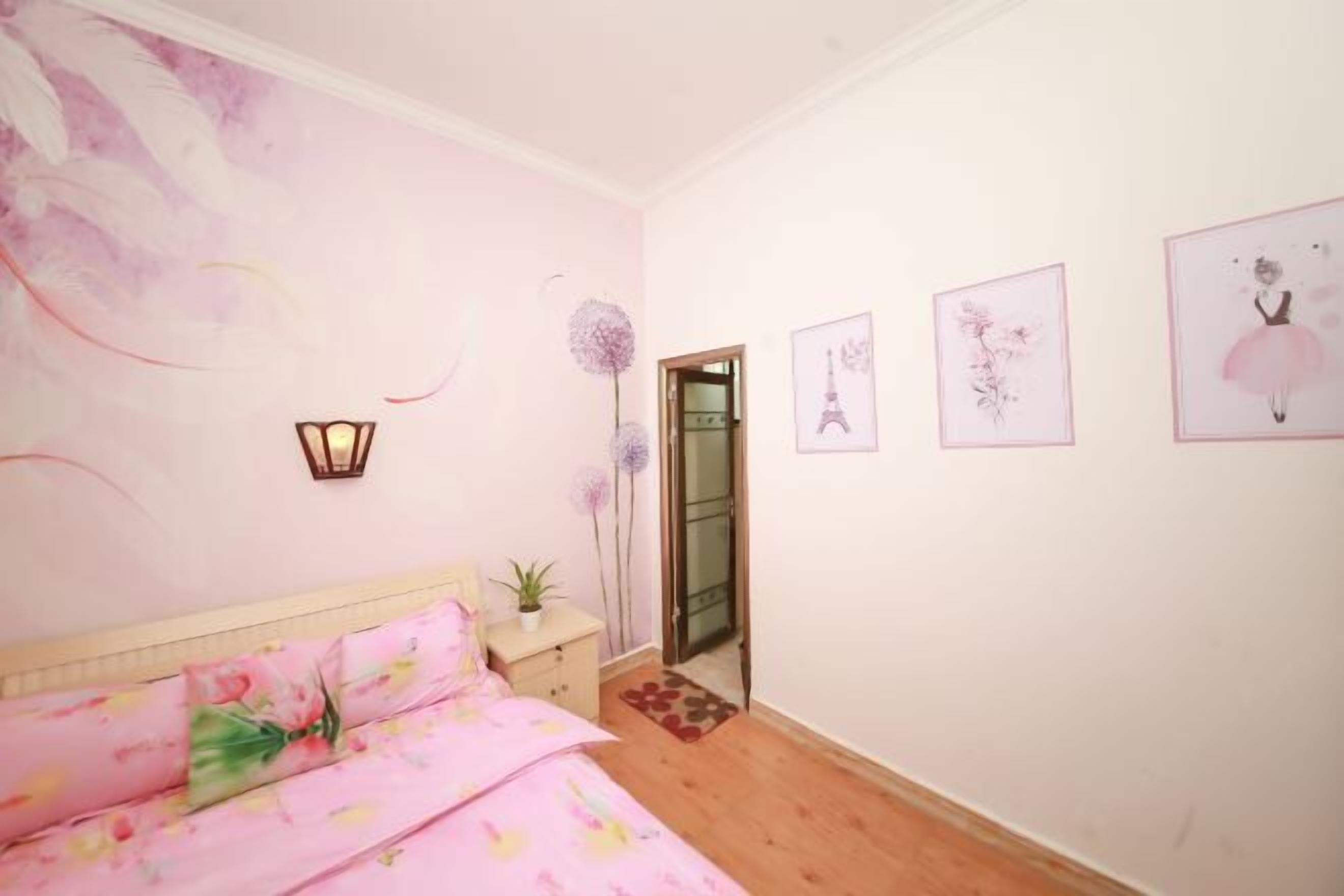 A bedroom with a bed, a nightstand, a potted plant, and a door leading to another room.
