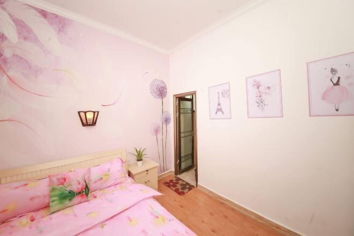 A bedroom with a bed, a nightstand, a potted plant, and a door leading to another room.