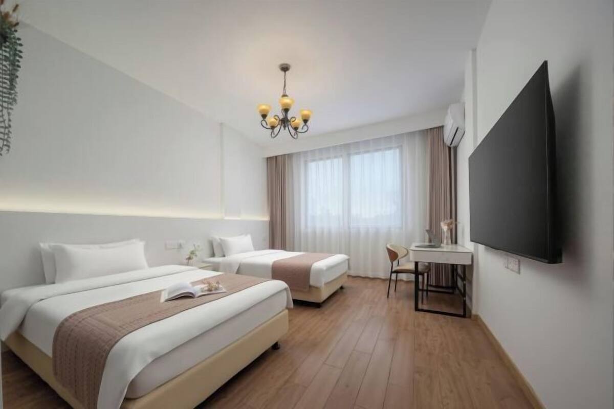A hotel room with two beds, a desk, a TV, and a chandelier.