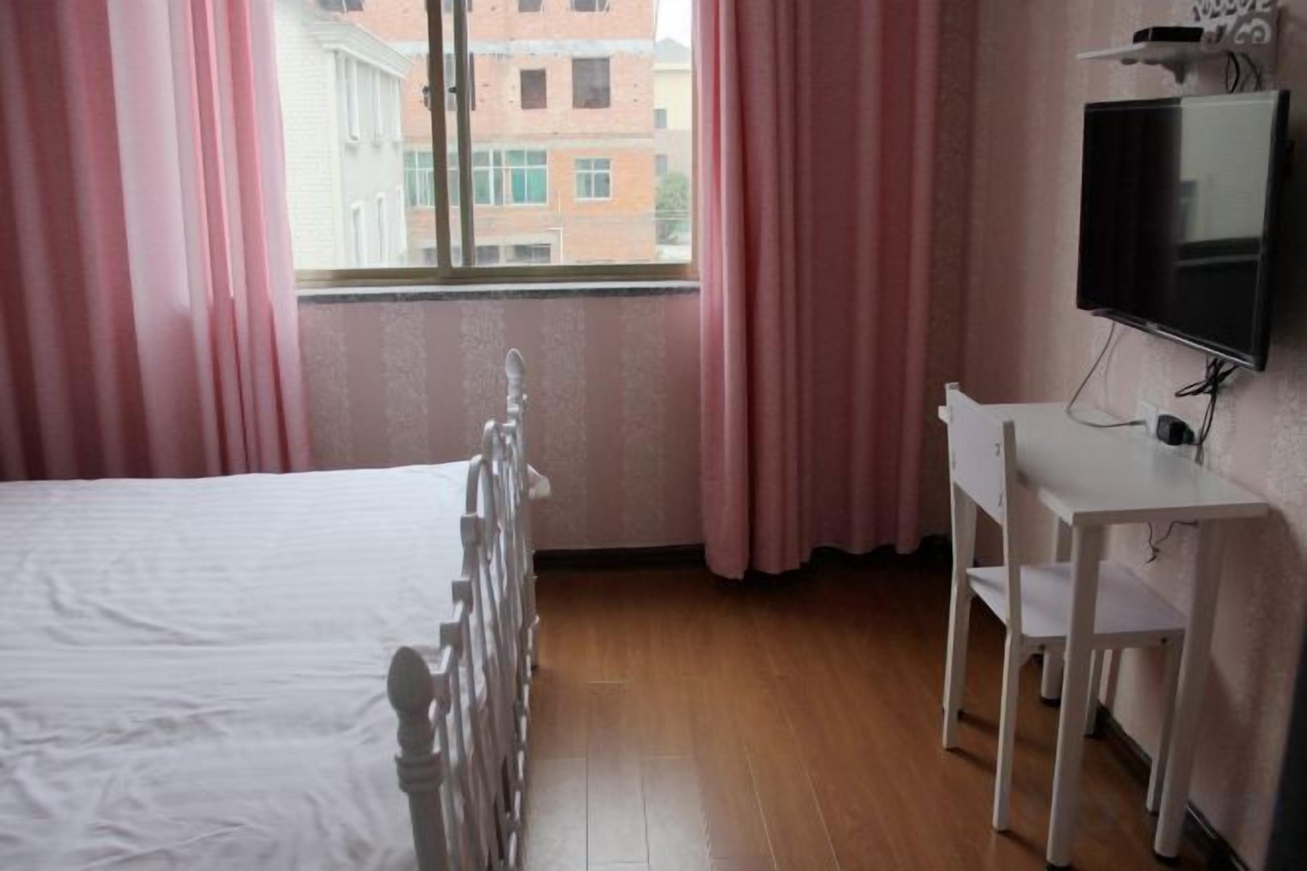 A room with a bed, a desk, a chair, a television, and a window with curtains.