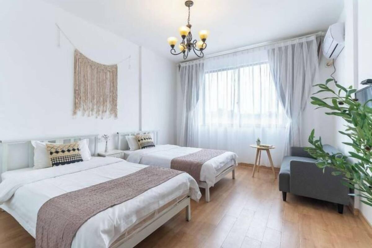 A room with two beds, a small table, a chair, a plant, and a chandelier.