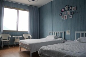 Una habitación con dos camas, una mesita y sillas. Hay una ventana con cortinas, y una pared decorada con cuadros.