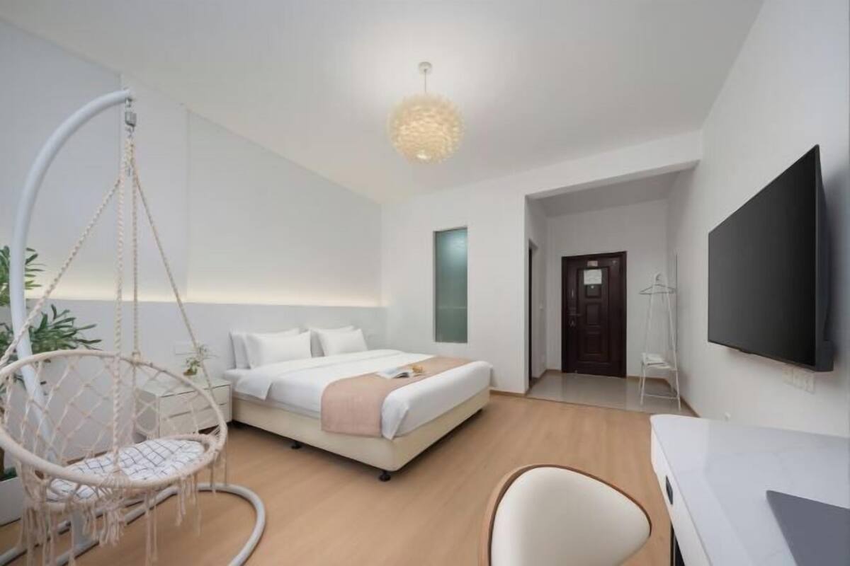 A modern hotel room with a bed, a hanging chair, a desk, and a TV.