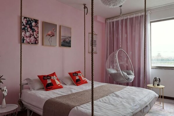 A bedroom with a bed, two pillows, a hanging chair, a small table, and a window with curtains.