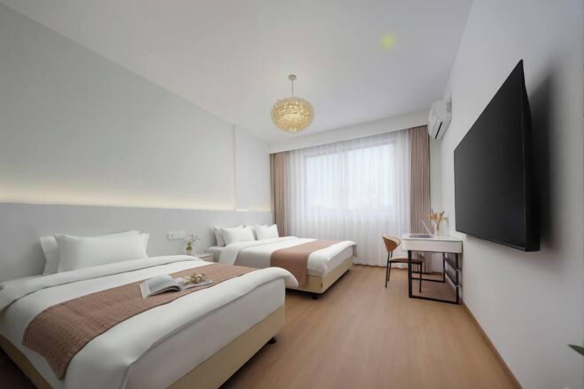 A hotel room with two beds, a desk, a chair, a TV, and a window with curtains.