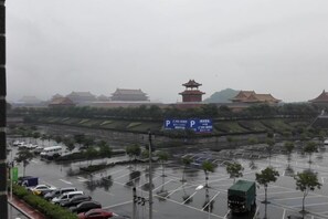 Um parque de estacionamento com veículos, um edifício tradicional com telhado em estilo pagode, e uma placa com caracteres chineses.
