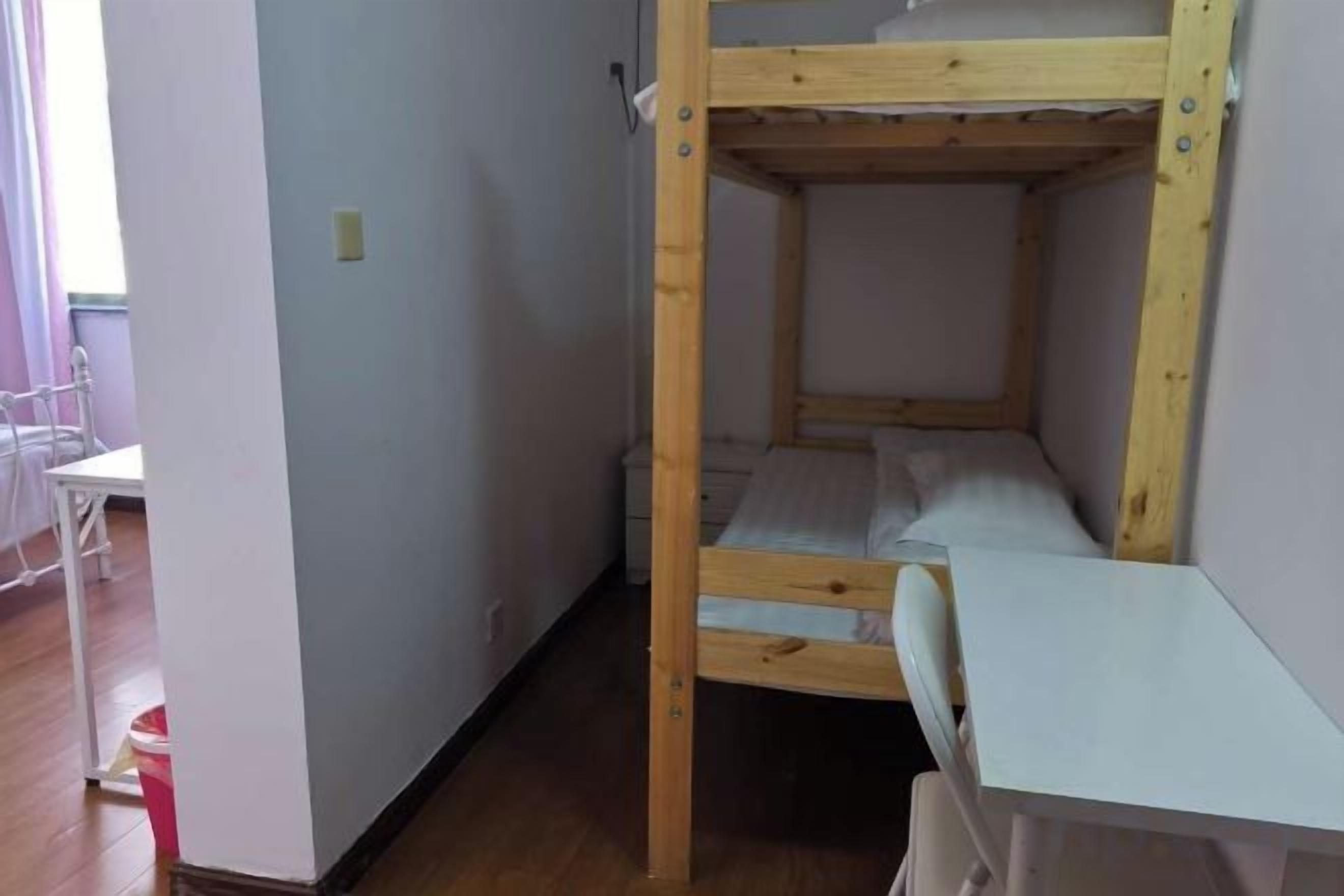 A bunk bed with a desk and chair, a white wall, and a wooden floor.