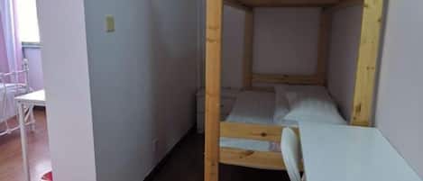 Een stapelbed met een bureau en stoel, een witte muur en een houten vloer.