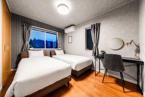 A hotel room with two beds, a desk with a chair, a window with curtains, and an air conditioning unit. - THE GRACIOUS (Sapporo)