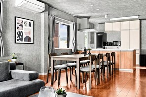 A modern kitchen with a central island, wooden flooring, and a dining area with a table and chairs. - THE GRACIOUS (Sapporo)
