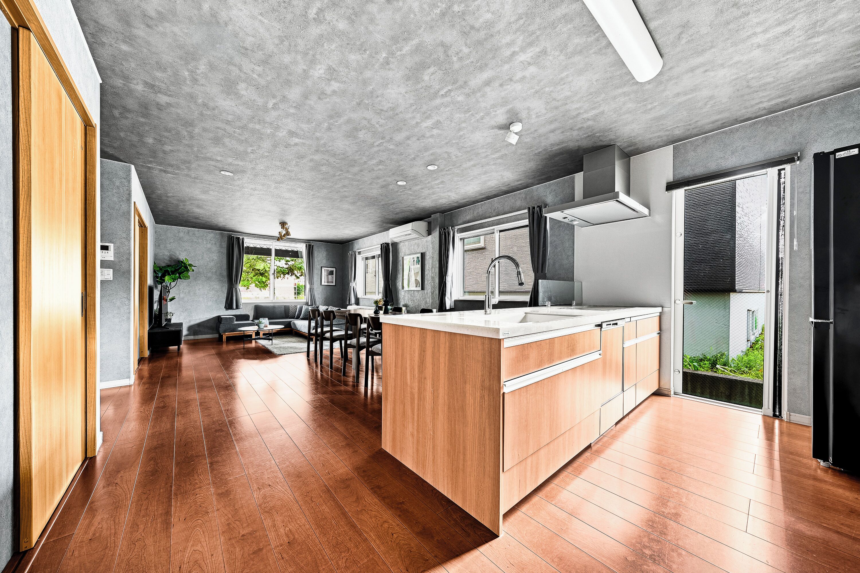 Una cocina moderna con una isla de madera, un comedor con sofá y sillas, y vistas a zonas verdes.