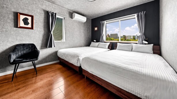 A modern bedroom with two beds, a chair, and a large window with a city view. - THE GRACIOUS (Sapporo)