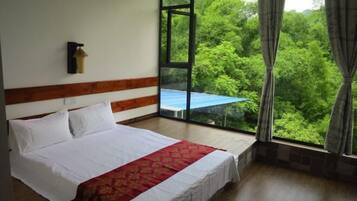 A bedroom with a bed, a window with a view of greenery, and a wall-mounted light fixture.
