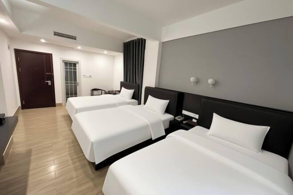 A hotel room with three beds, a dark headboard, a wooden floor, a door, and a window with curtains.