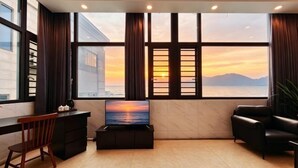 Una habitación moderna con un ventanal grande, un televisor de pantalla plana, un escritorio, una silla y un sofá.