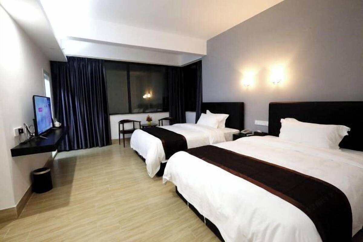 A hotel room with two beds, a desk with a computer, a small table, and a window with curtains.