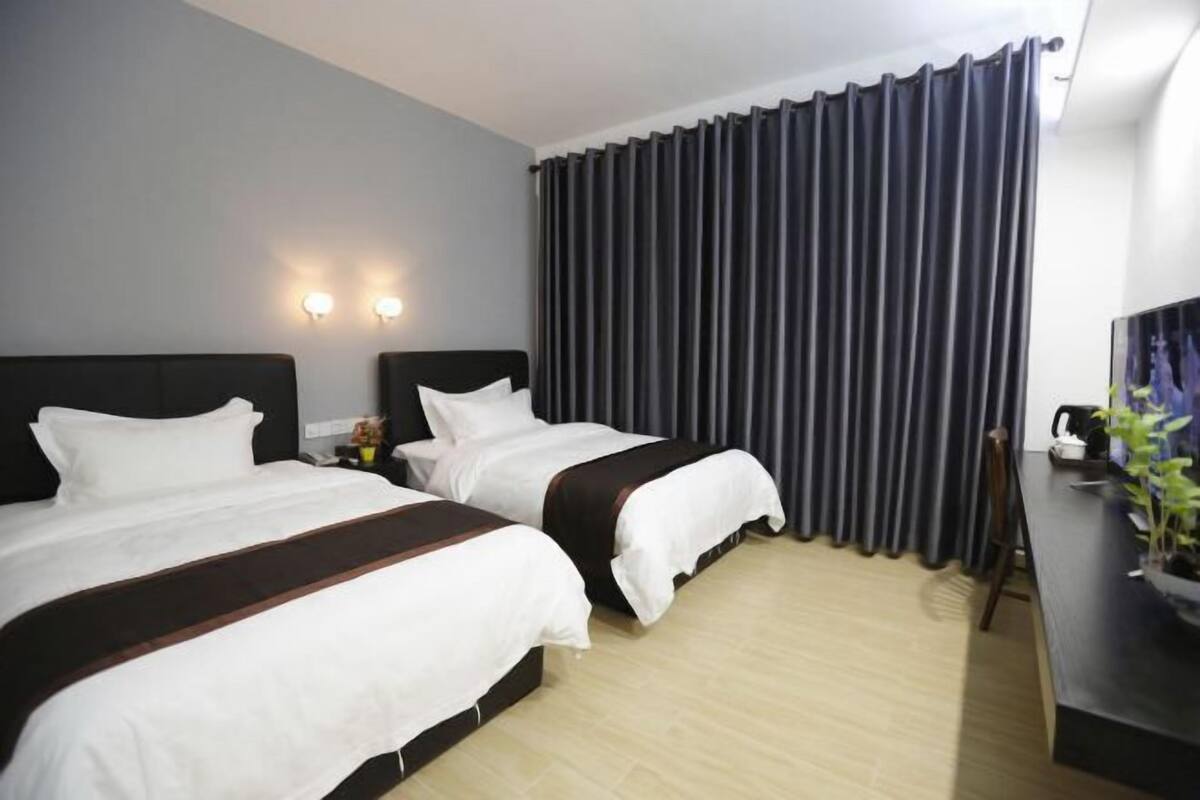 A hotel room with two beds, a desk, a chair, and a large window with curtains.