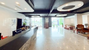 Un lobby moderno de hotel con un mostrador de recepción de mármol, luces de techo circulares y vistas al exterior.