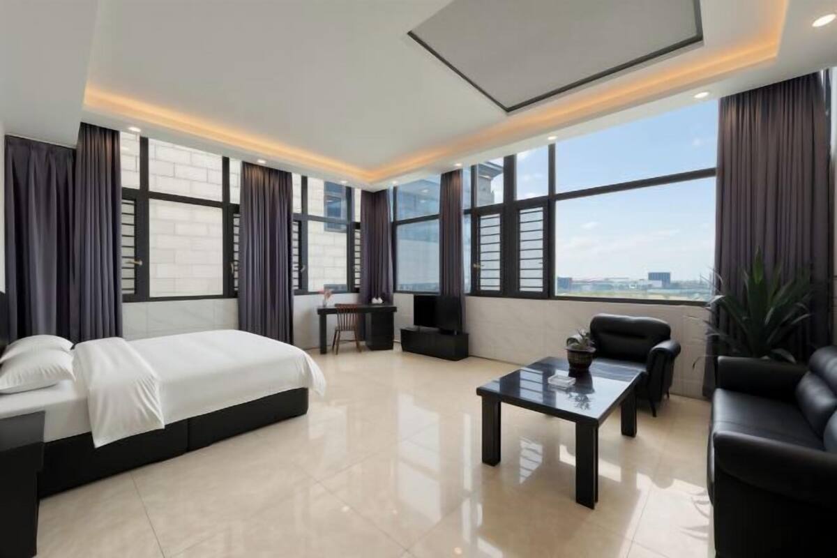 A modern hotel room with a large bed, a desk, a coffee table, and a sofa.