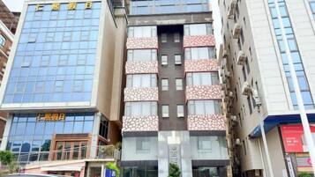 A multi-story building with a mix of glass and patterned facades, featuring a central entrance with a sign.