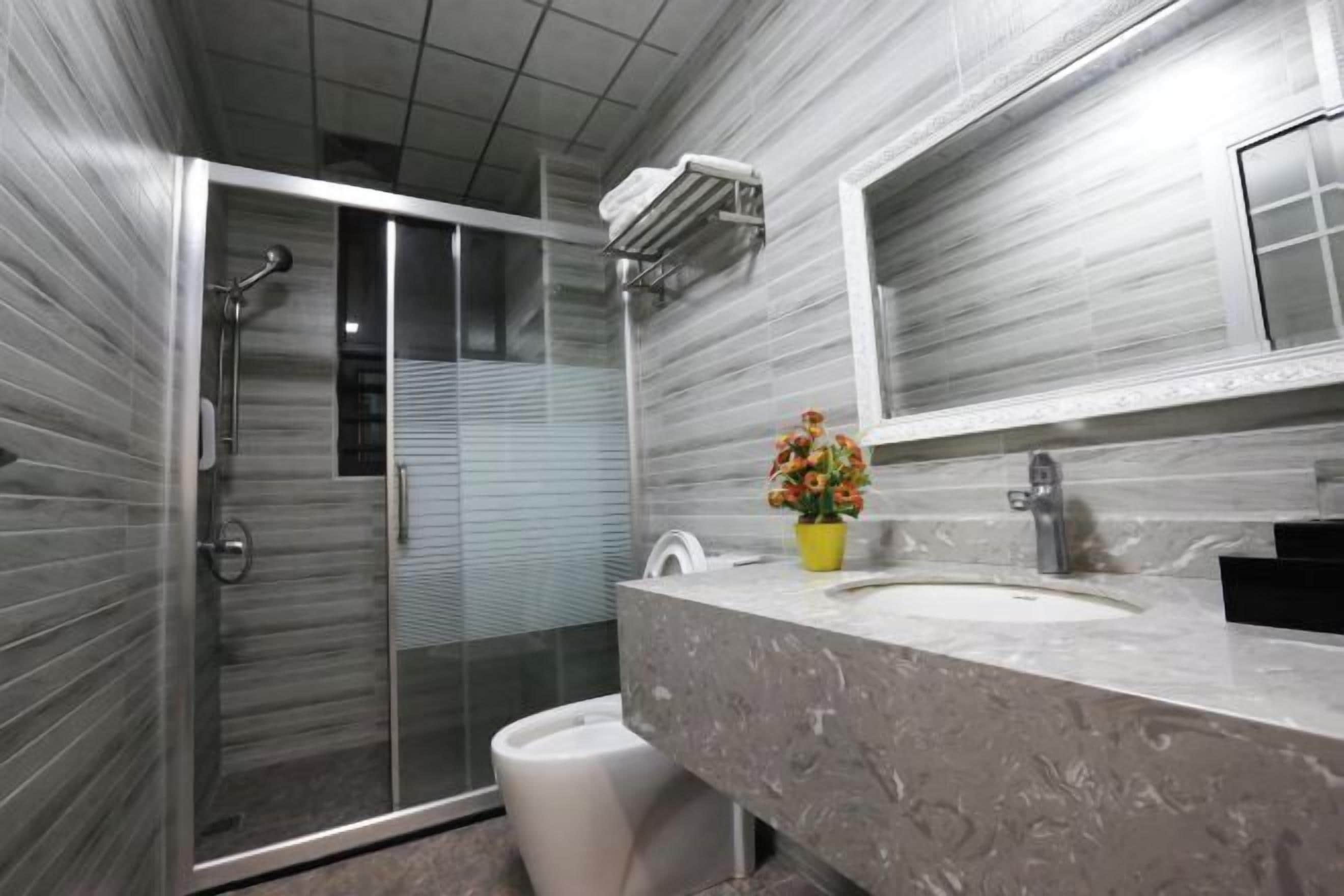 A modern bathroom with a glass-enclosed shower, a marble sink, and a potted plant.