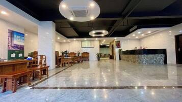 Een hotel lobby met een receptiebalie, een zithoek en een marmeren vloer.