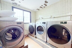 A laundry room with three front-loading washing machines, a window, and tiled walls.