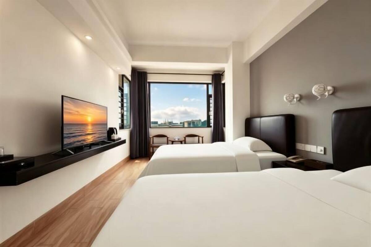 A hotel room with two beds, a TV, a desk, and a view of the city.