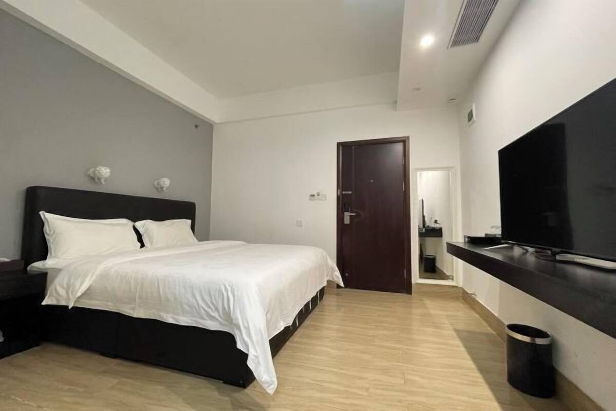 A bedroom with a bed, a TV, a door, and a small trash bin.