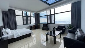 Una habitación de hotel moderna con una cama, un sofá, una mesa de centro y grandes ventanales con vista a la ciudad.