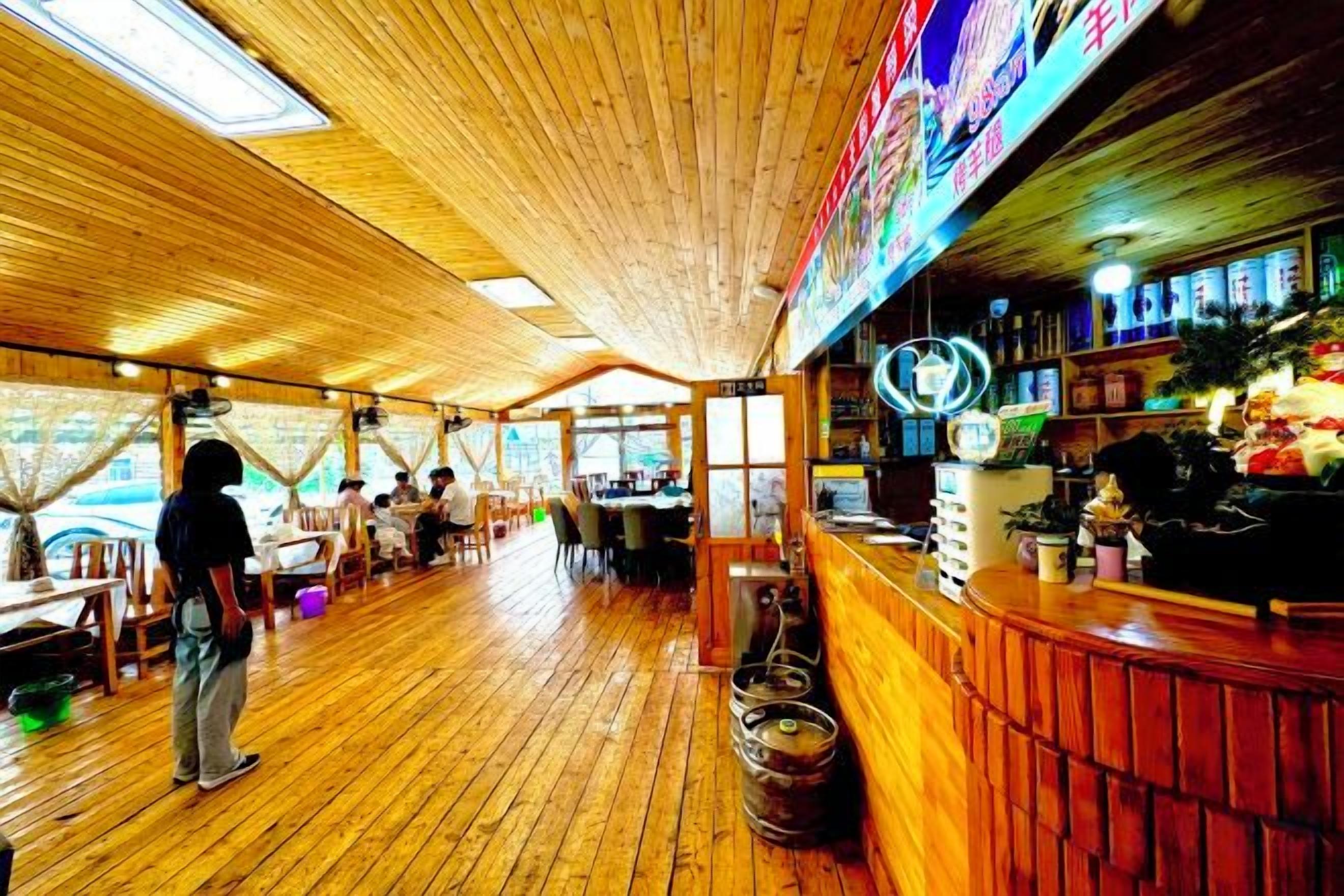 An indoor restaurant with wooden flooring, tables, and a bar area with stools.