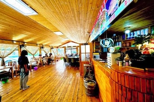 Ein Restaurant mit Holzboden, Tischen und einer Bar mit Hockern.