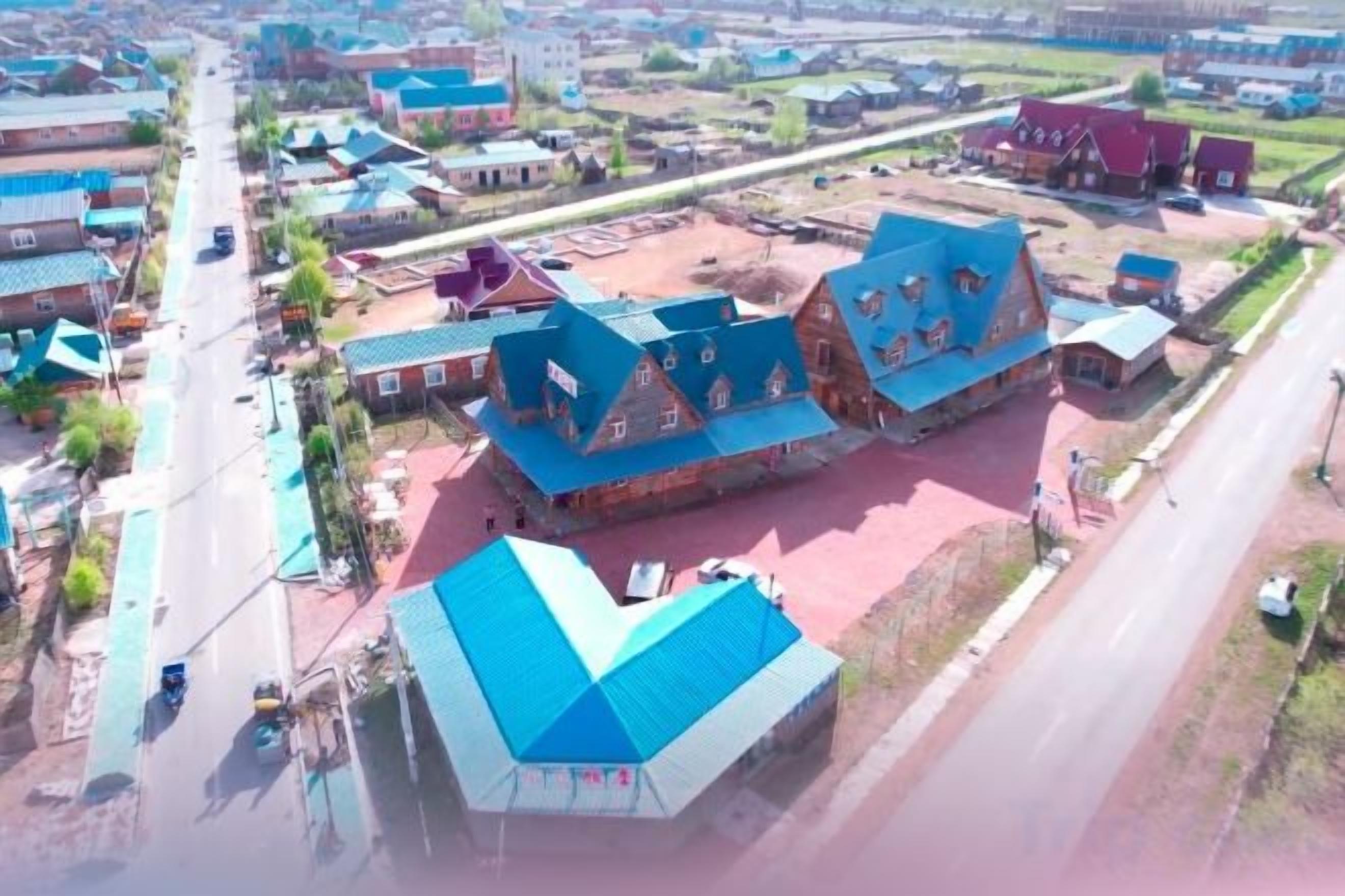 Zona rural con un edificio destacado de techo azul, rodeado de construcciones más pequeñas y una carretera.