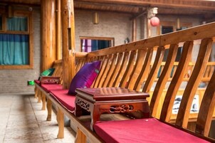 A row of wooden benches with red cushions in a rustic room with brick walls and wooden beams.
