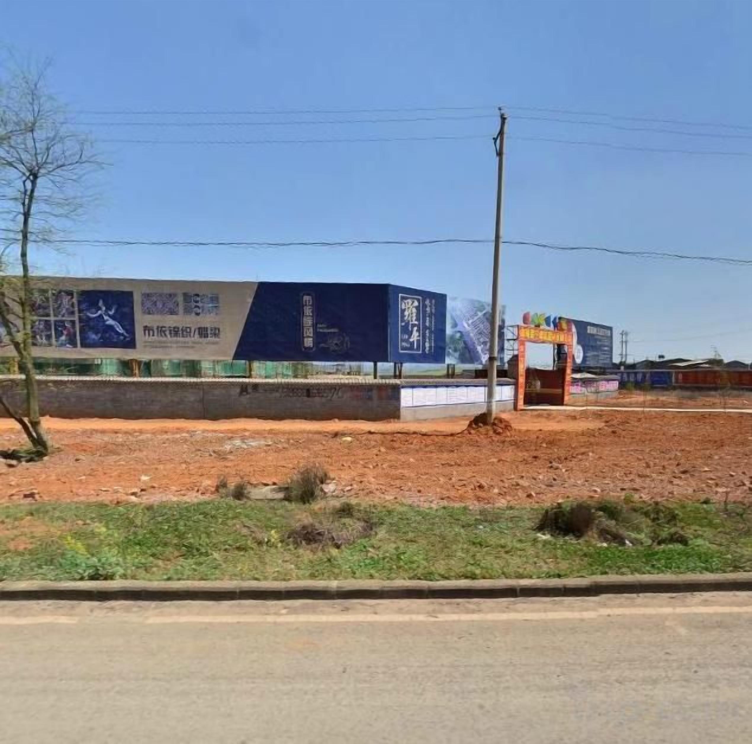 A construction site with a large blue banner, a small structure, and a dirt ground.